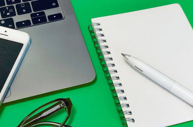 緑のテーブルの上にあるパソコンとメモ帳